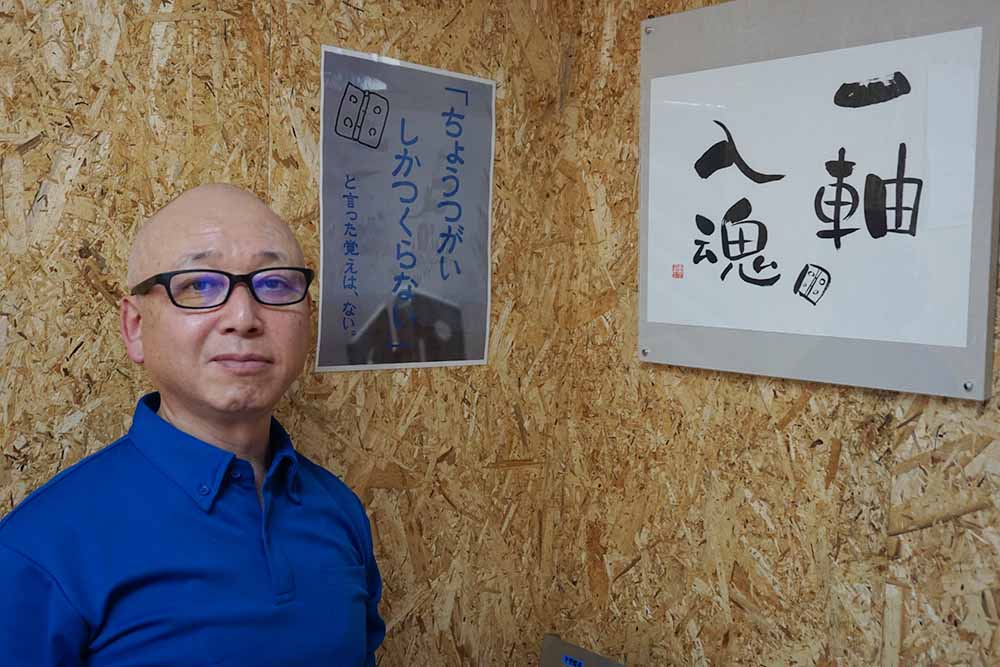 伊藤徹郎代表と、掲げられた「一軸入魂」の掛け軸